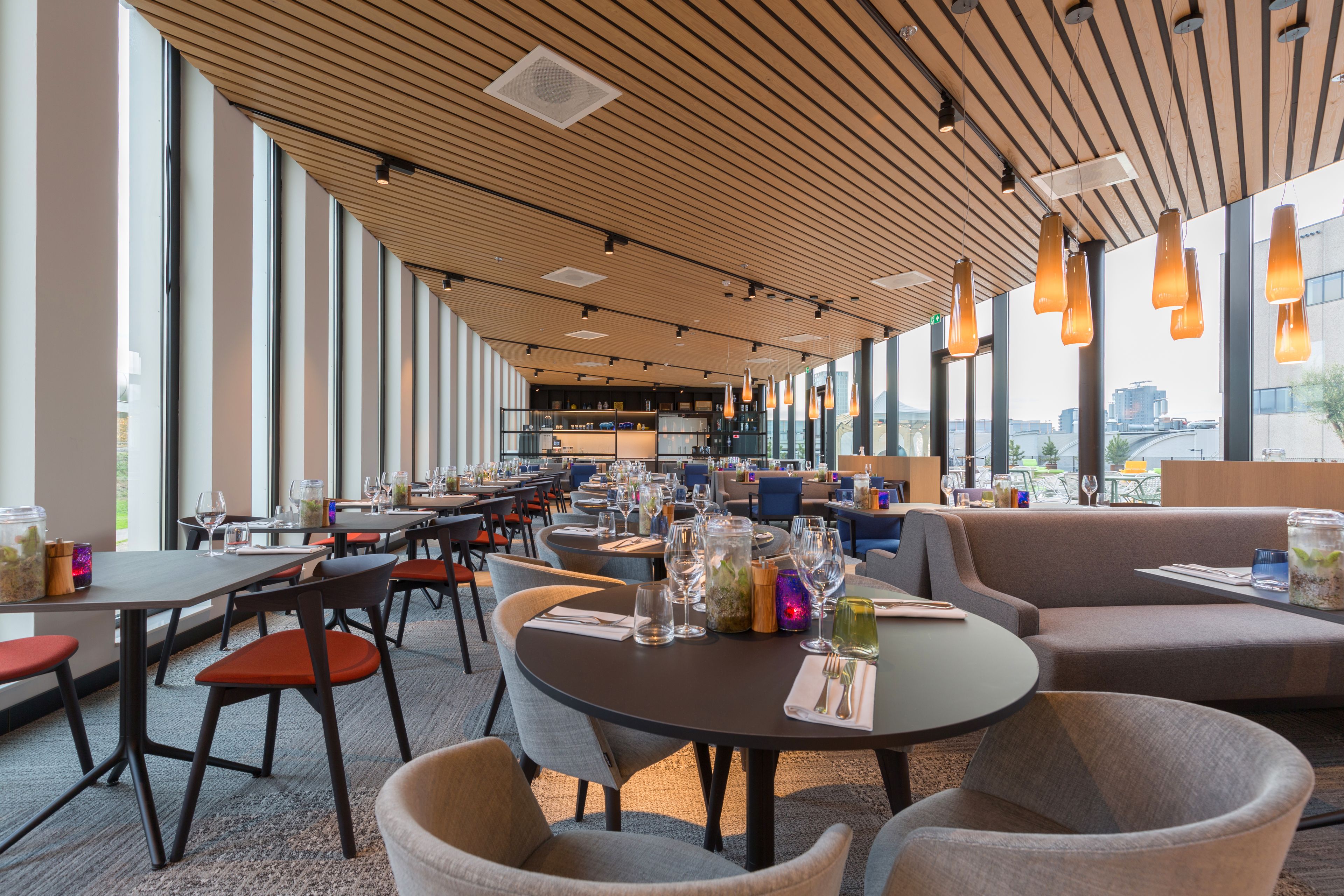 Un restaurante moderno con techos altos, grandes ventanales y diversas opciones de asientos, como mesas y cabinas.
