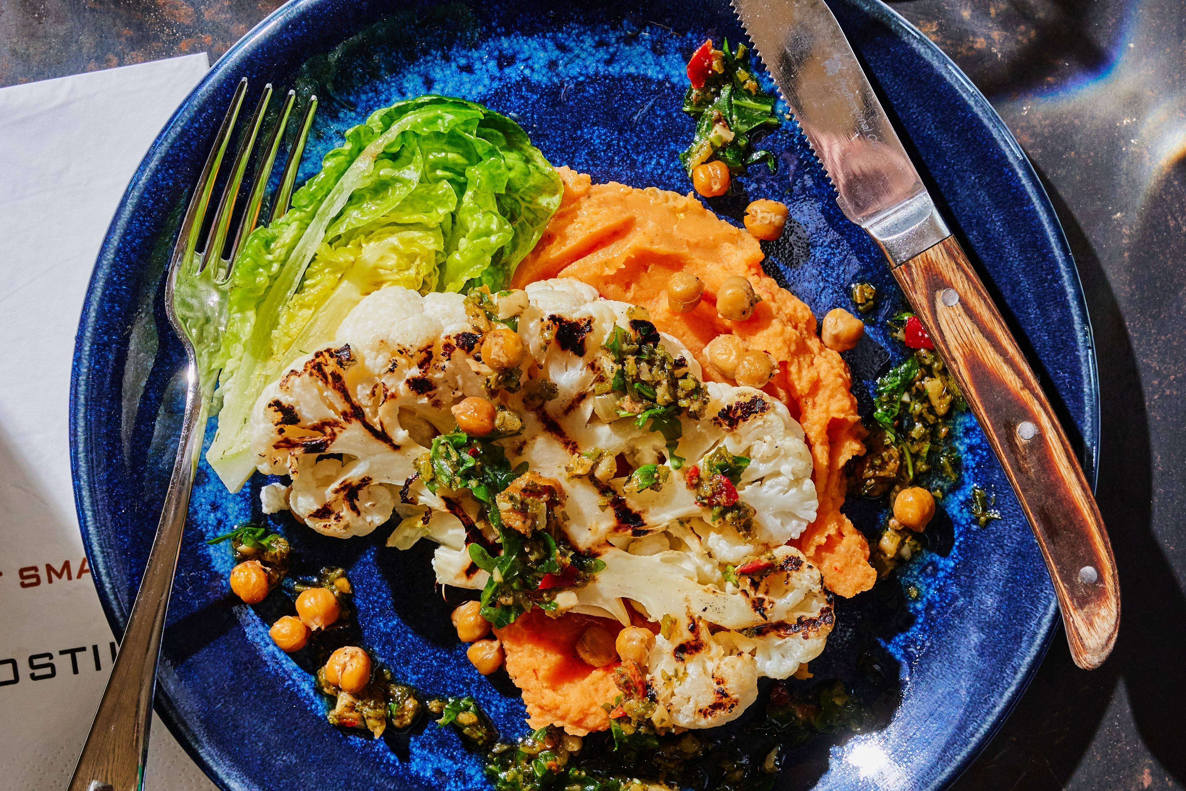 Un plato de comida con coliflor a la parrilla, garbanzos y una guarnición de vegetales verdes.