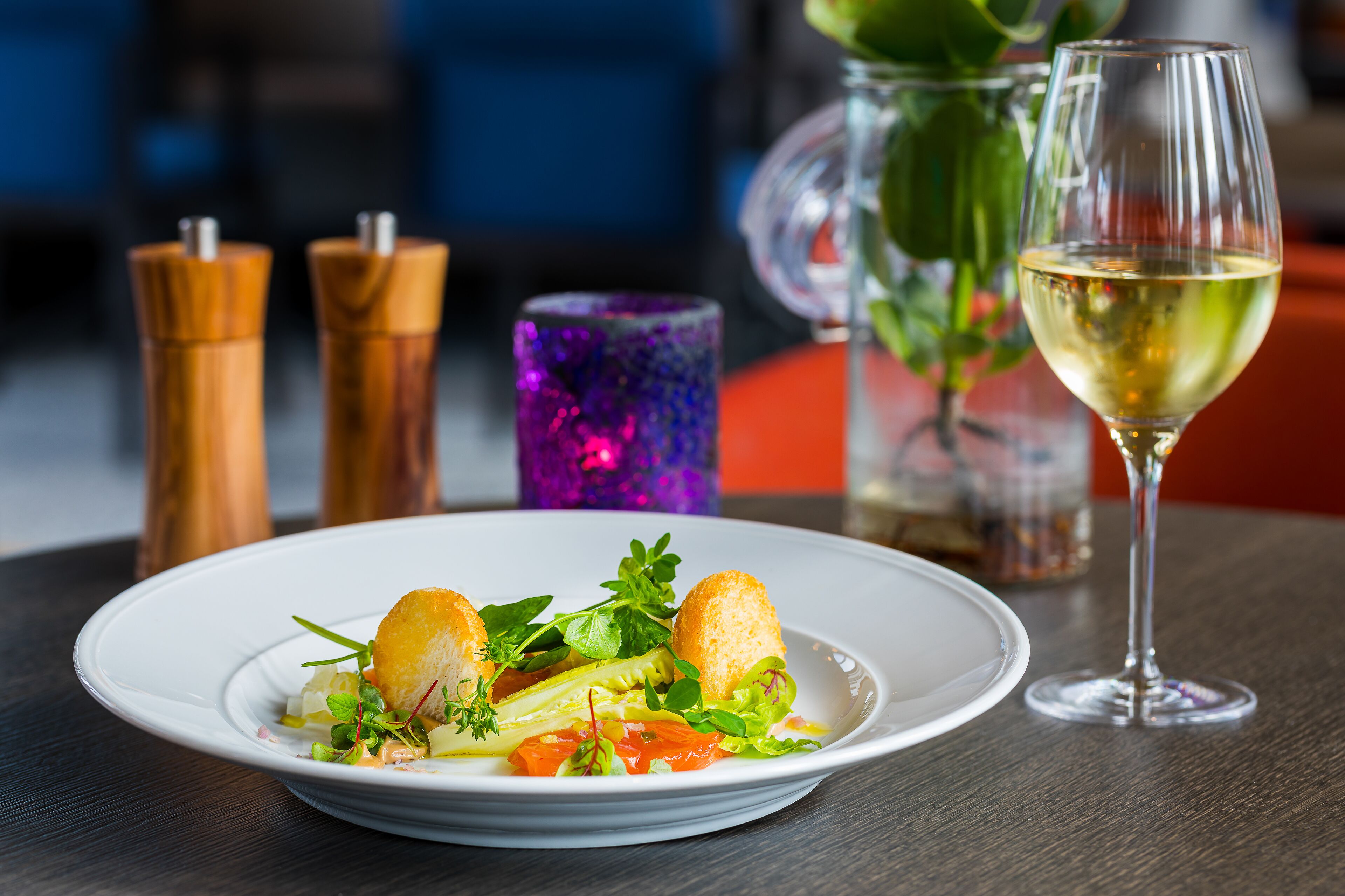 Un plato de comida con una copa de vino blanco sobre una mesa.