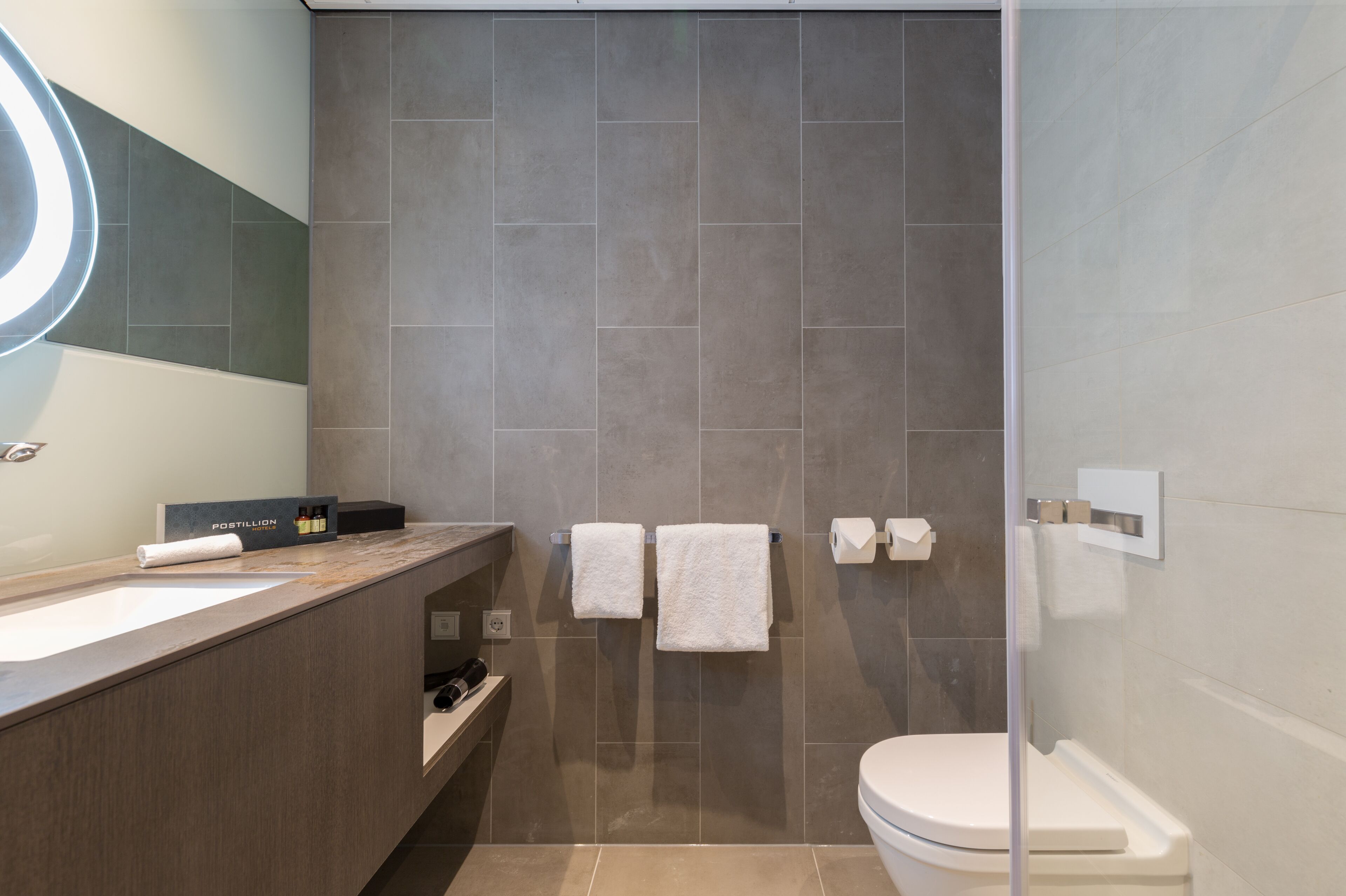 Une salle de bain moderne avec un grand lavabo, deux serviettes blanches, une douche en verre et des toilettes.