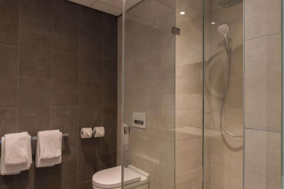 Une salle de bain moderne avec une douche à parois de verre, des toilettes et deux serviettes blanches suspendues à un porte-serviettes.