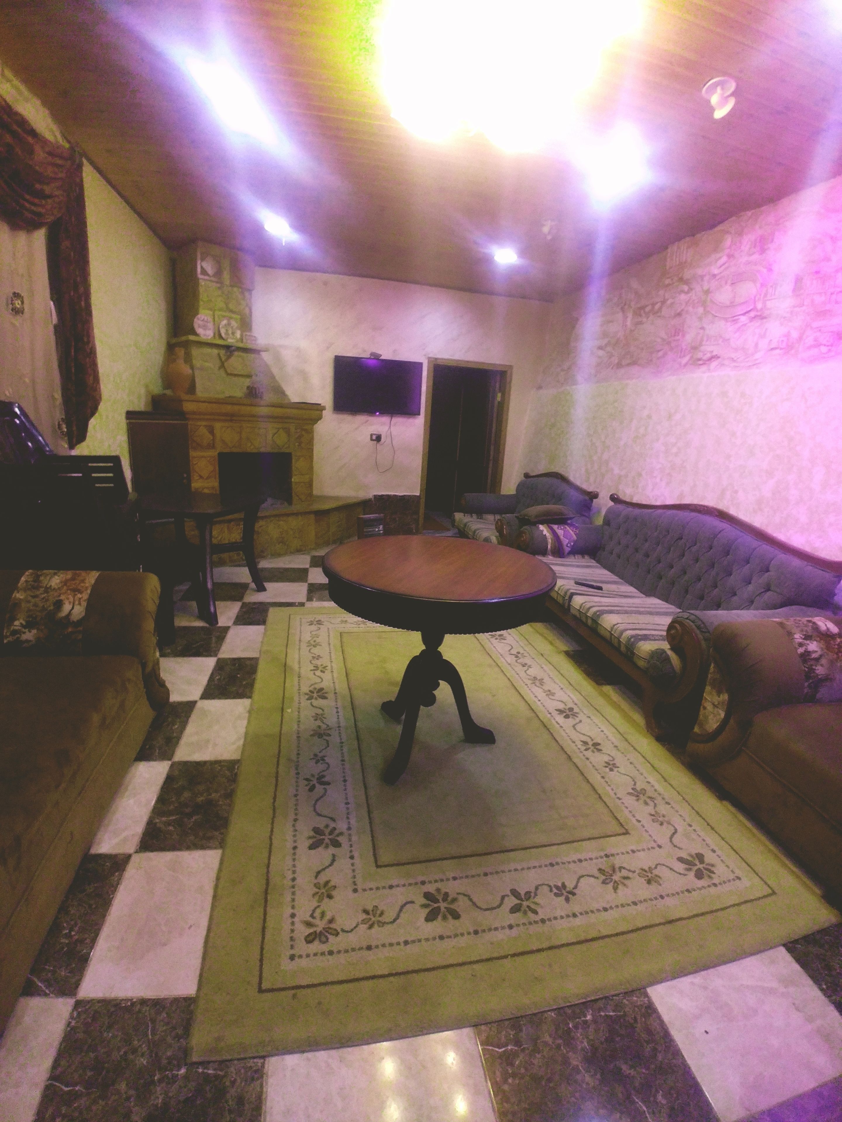 A living room with a checkered floor, a round table, a sofa, and a television mounted on the wall.