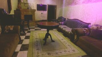 A living room with a checkered floor, a round table, sofas, and a television on the wall.