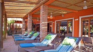 A covered outdoor lounge area with wicker lounge chairs and blue cushions, brick pillars, and a tiled floor. - Bella Ilha Pousada (Ilhabela)