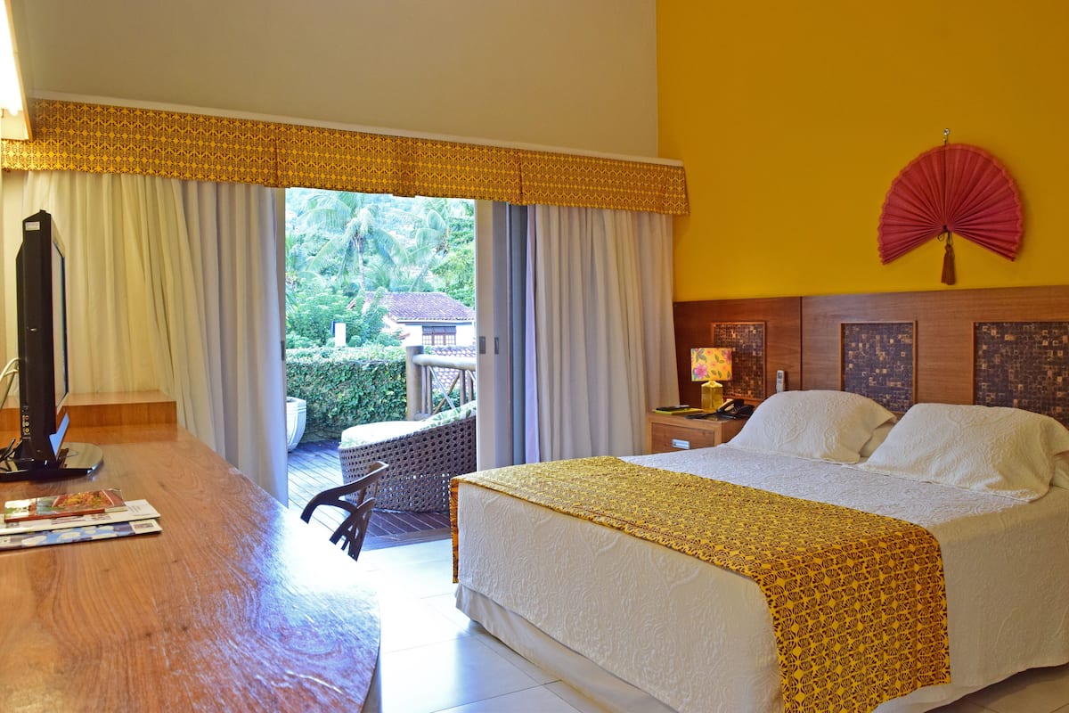 Une chambre d’hôtel avec un grand lit, un bureau en bois, une chaise, une table de chevet et une vue sur l’extérieur.