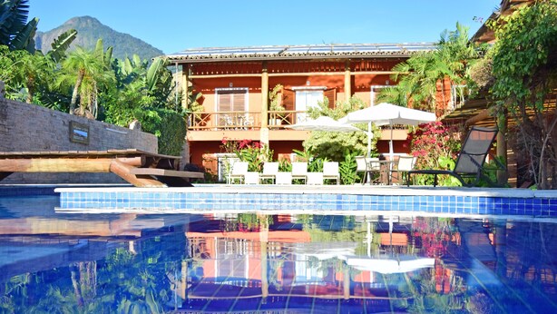 A hotel with a swimming pool, outdoor seating, and lush greenery. - Bella Ilha Pousada (Ilhabela)