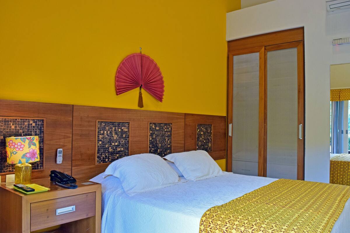 Une chambre d’hôtel avec un lit, une tête de lit en bois, une table de chevet avec une lampe, un téléphone et un éventail décoratif.