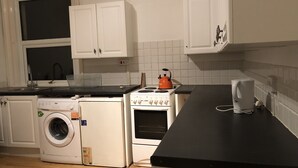 A kitchen with white cabinets, a washing machine, a stove, and a kettle. - 2 Bed Apartment in Basingstoke (Basingstoke)