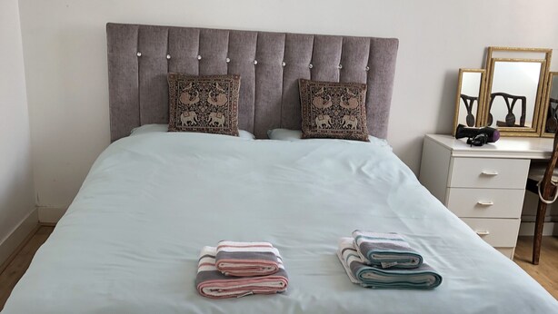 A neatly made bed with a grey headboard, two decorative pillows, and folded towels on the bed. - 2 Bed Apartment in Basingstoke (Basingstoke)