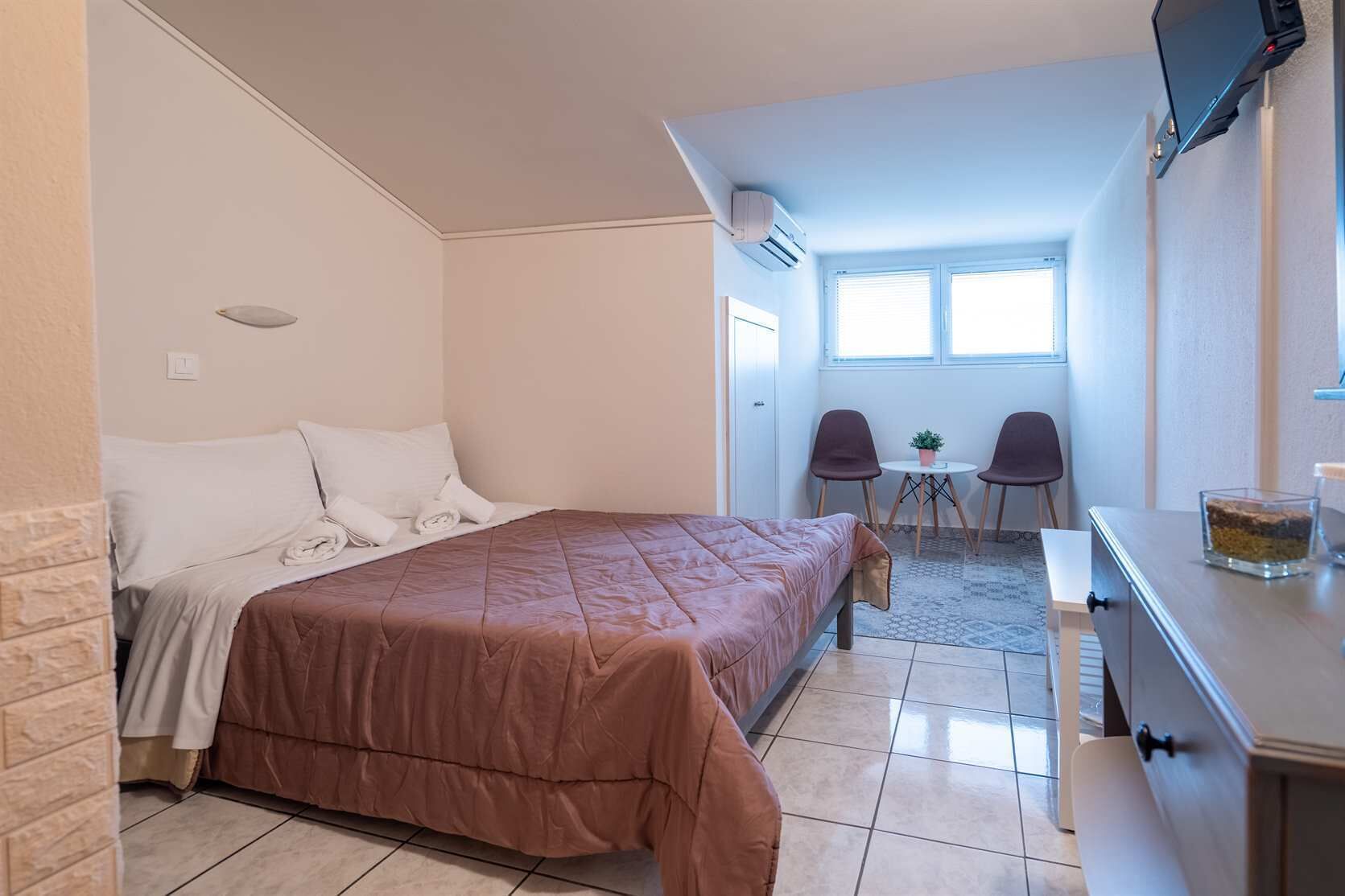Un dormitorio con cama, escritorio, dos sillas y una mesita con una planta.