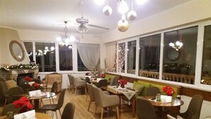 Comedor con varias mesas y sillas, ventanas amplias con cortinas y una chimenea decorada.