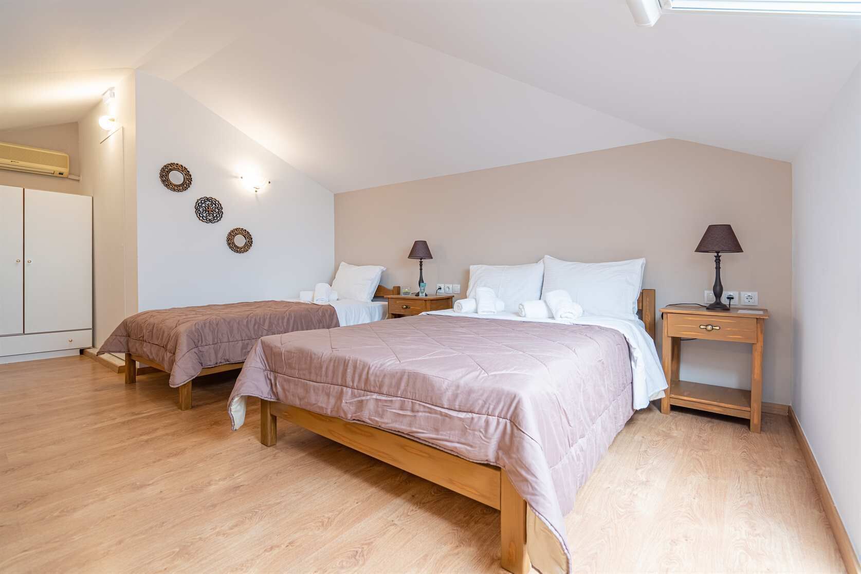 A bedroom with two single beds, wooden flooring, a wardrobe, and bedside tables with lamps.