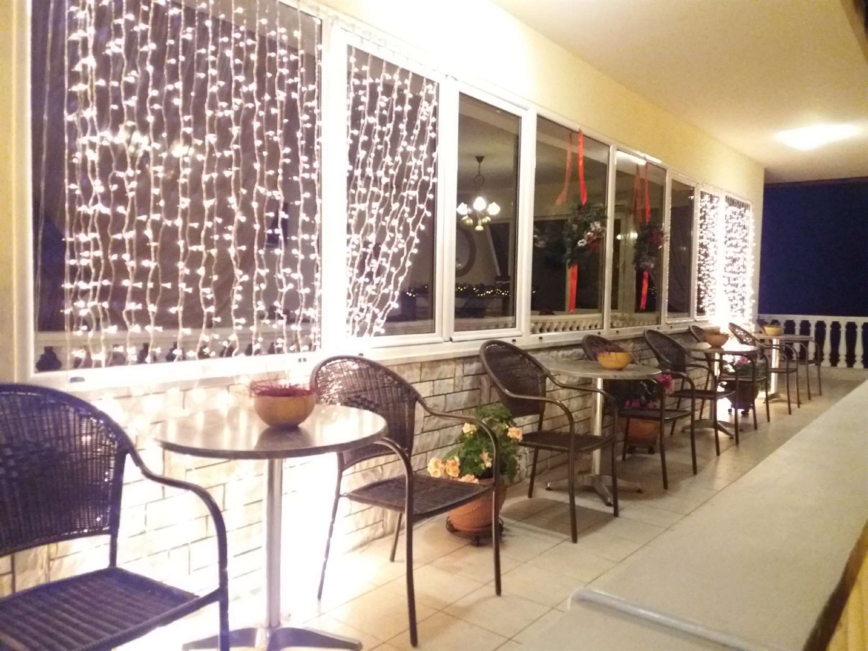 Un espacio al aire libre con mesas y sillas, decorado con luces colgantes y plantas en macetas.