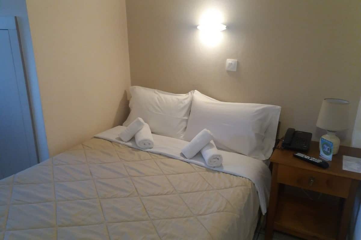 Ein Hotelzimmer mit einem Bett, Kissen, einem Nachttisch mit Lampe, Telefon und Fernbedienung.