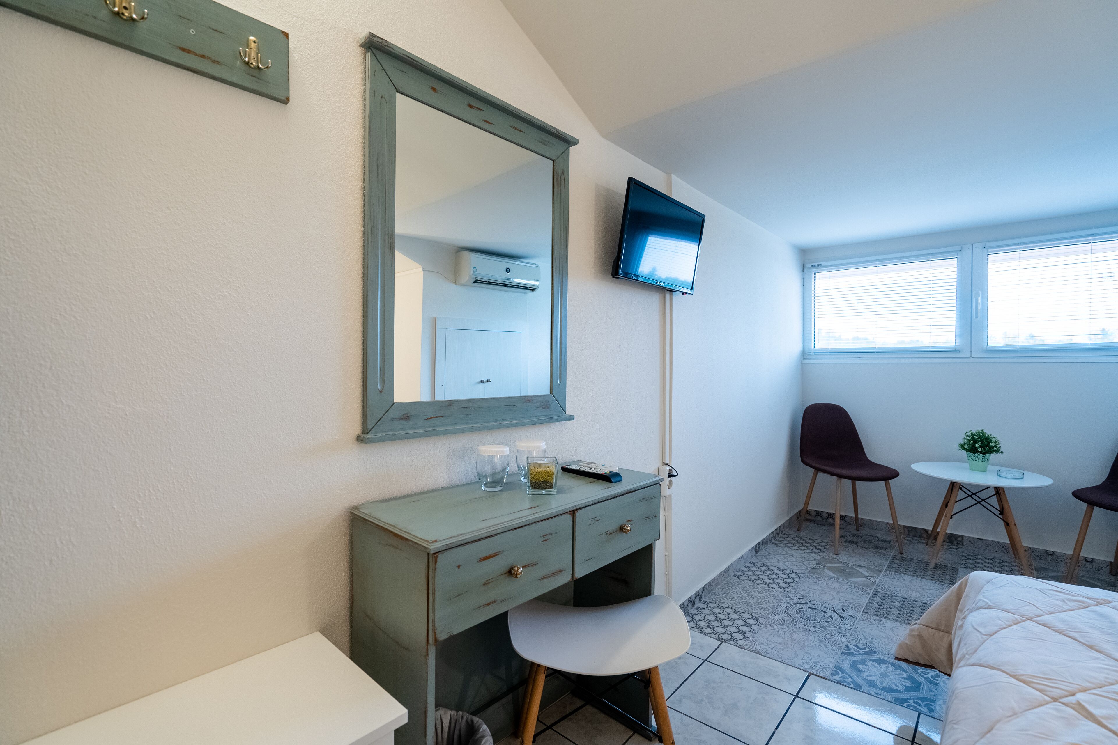 A bedroom with a bed, a desk, a chair, a small table, a TV, and a window.