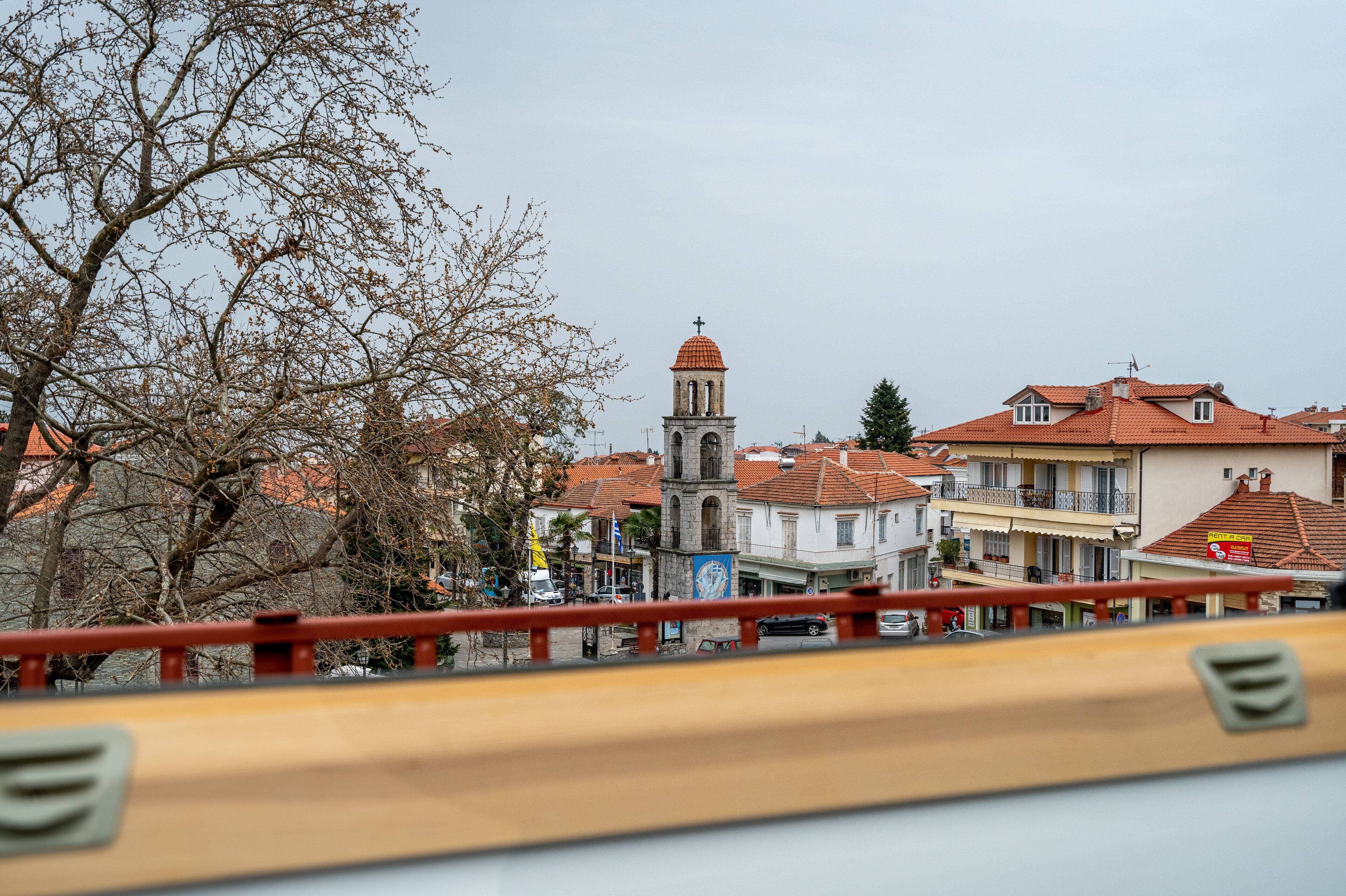 Un pueblo con una imponente torre de iglesia, edificios tradicionales y una barandilla de puente en primer plano.