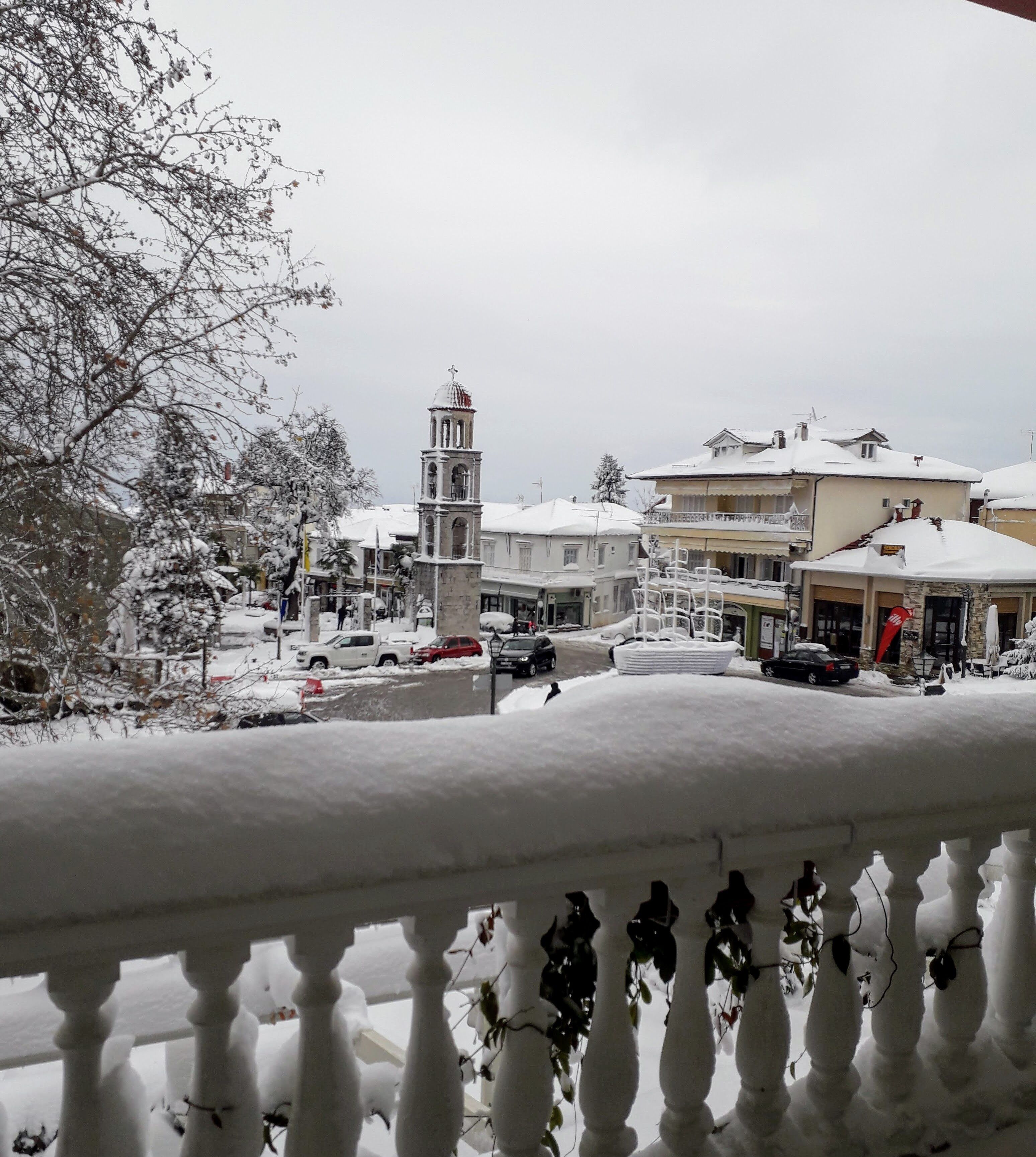 A snowy town square with a prominent clock tower, buildings with snow-covered roofs, and a clear view of the surrounding area.