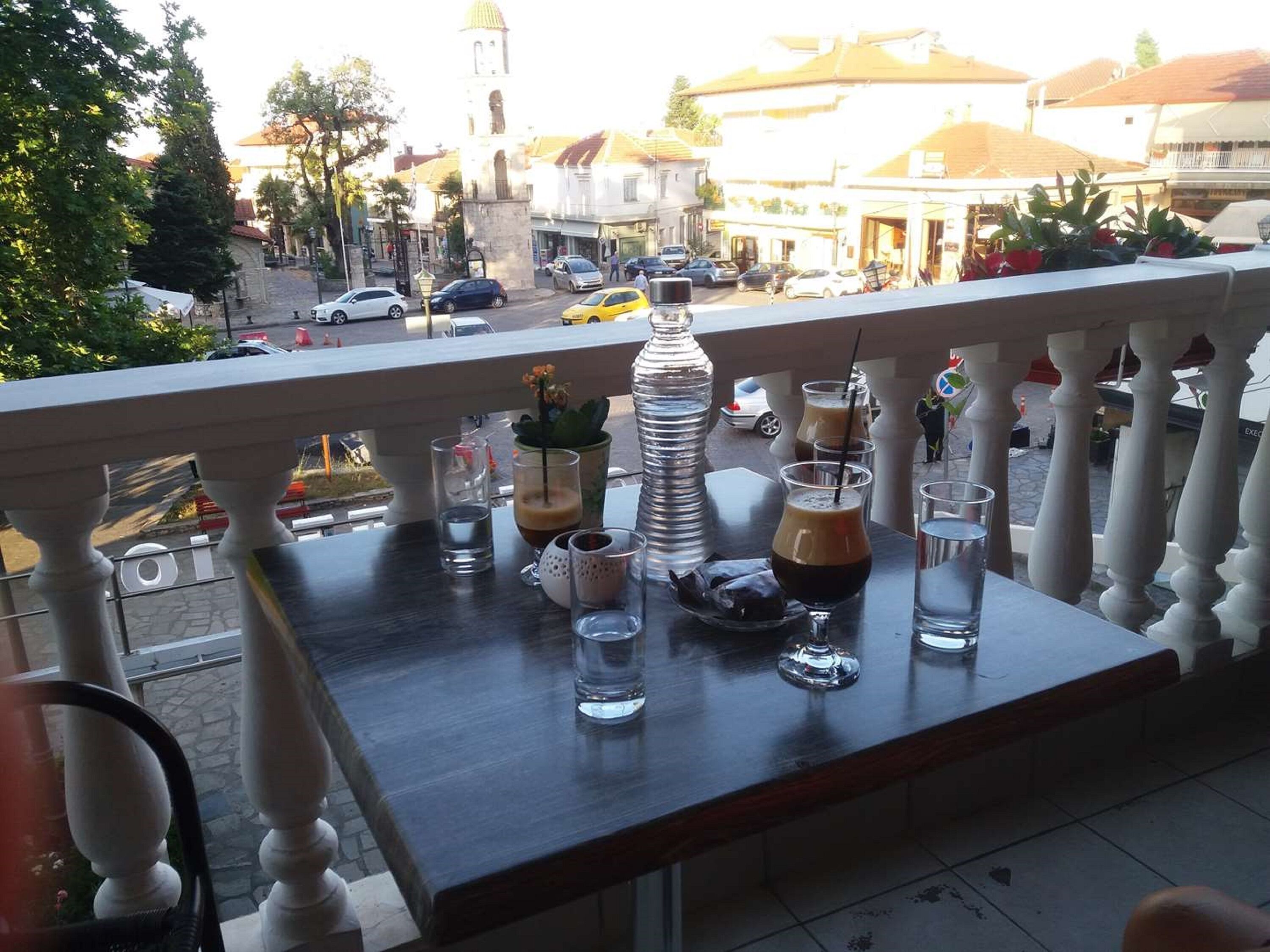 A balcony with a table set for drinks, overlooking a street with cars and buildings.