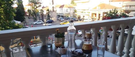 A balcony with a table set for drinks, overlooking a street with cars and buildings.