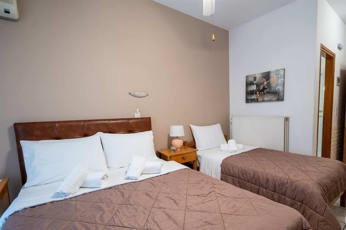 Ein Hotelzimmer mit zwei Betten, jeweils mit brauner Steppdecke und weißen Bettwäsche. An einem Nachttisch steht eine Lampe und ein kleines dekoratives Objekt. An der Wand ist ein Gemälde zu sehen, und ein Heizkörper ist an der Wand montiert.