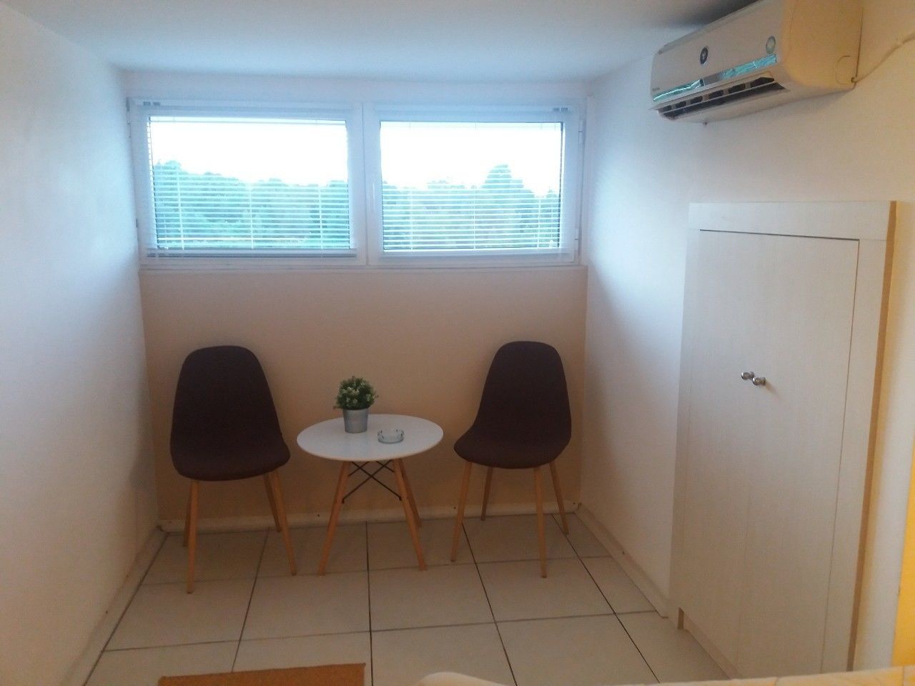 Een kleine kamer met twee stoelen, een tafeltje en een raam met zonwering.