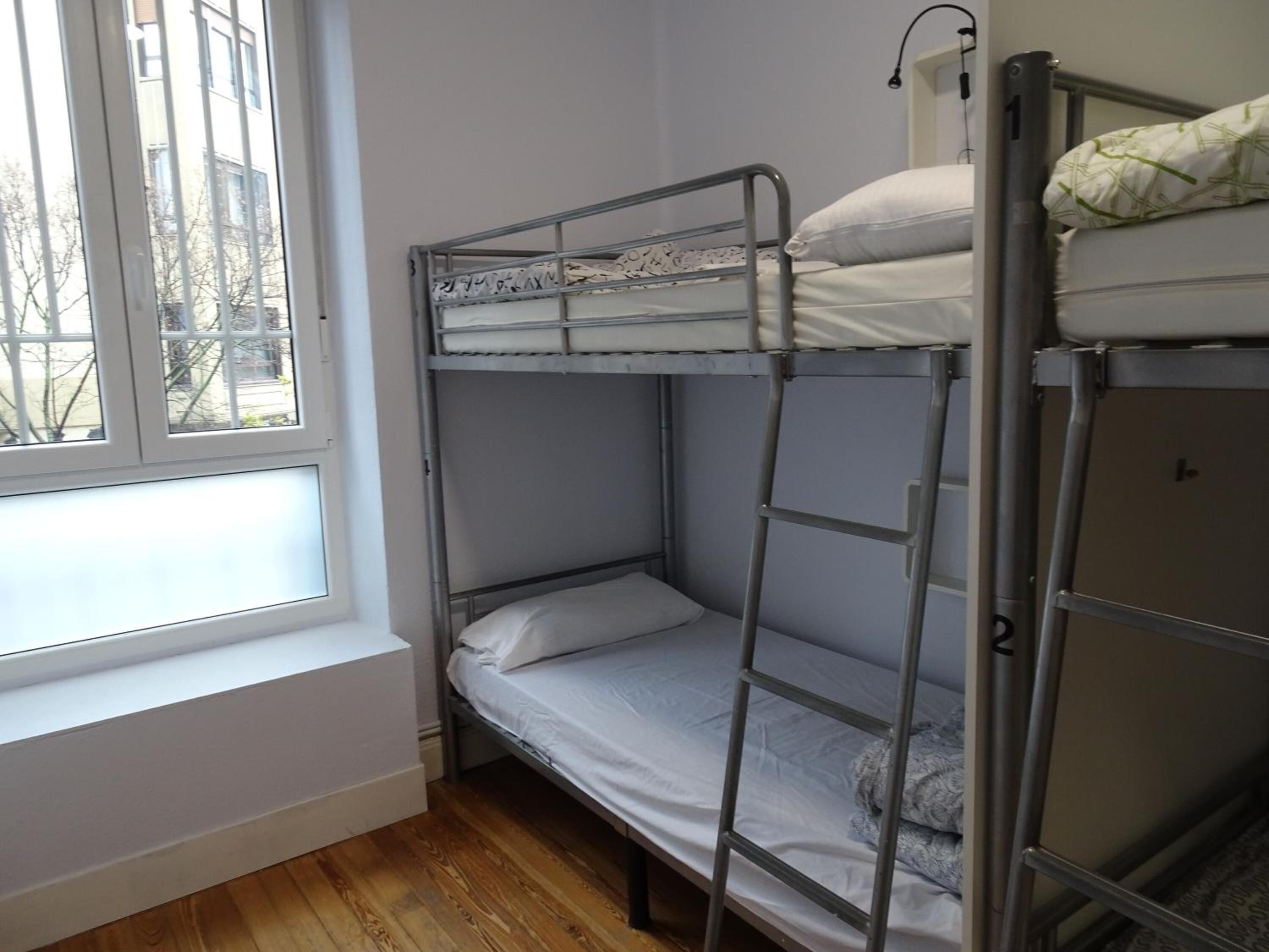 Habitación con literas, ventana, suelo de madera y escalera metálica.