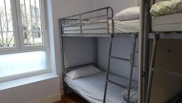 Habitación con literas, ventana, suelo de madera y escalera metálica.