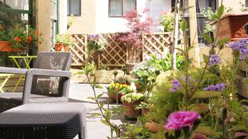 Een terras met rieten stoelen en tafels, omringd door potplanten en bloemen.