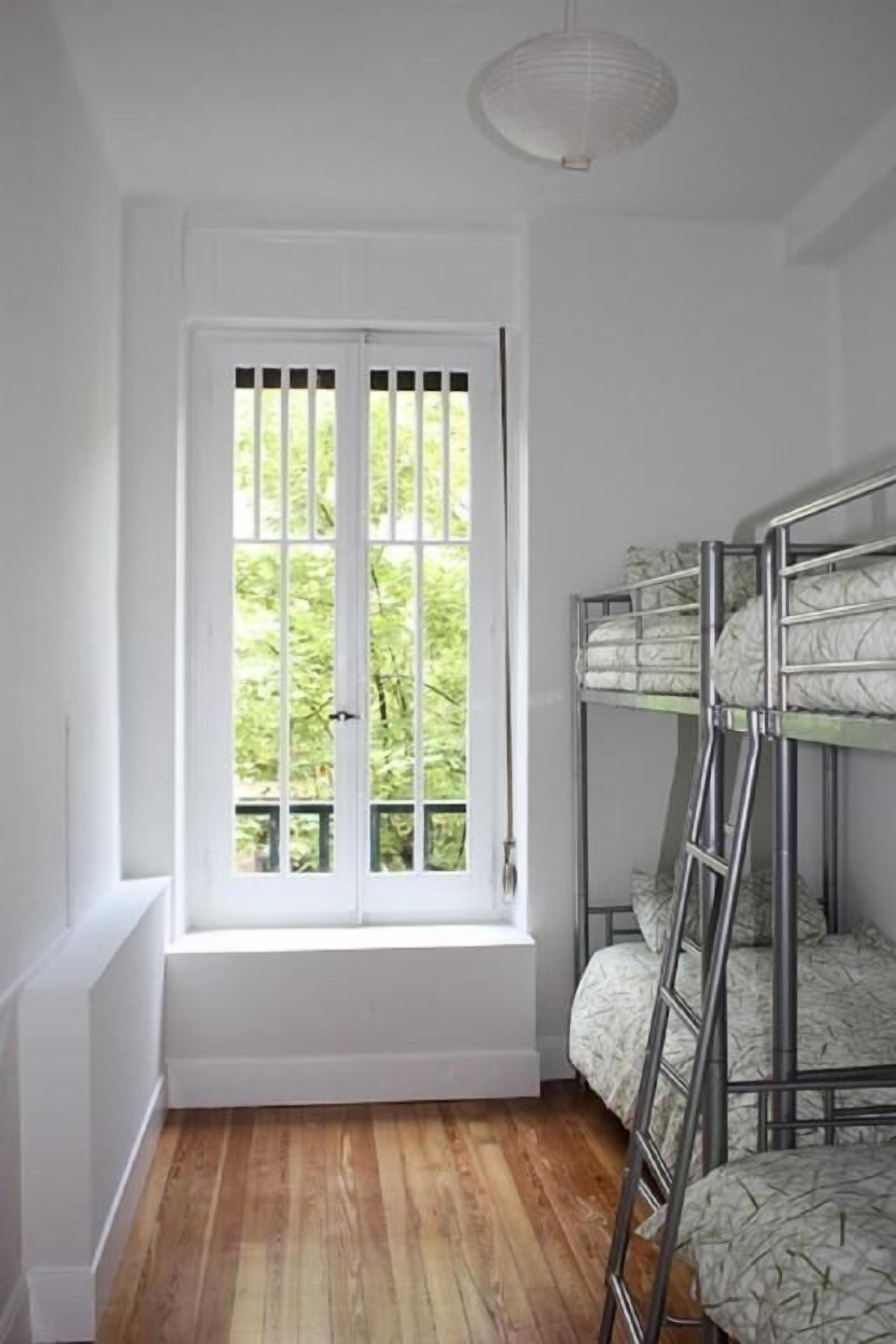 A room with bunk beds, a white door, and a window with a view of greenery.