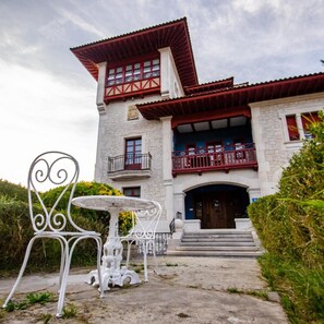 A two-story building with a stone facade, red balconies, and a central entrance with steps.