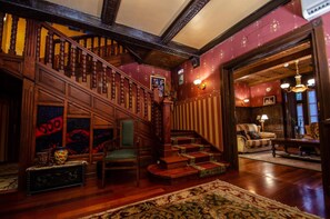 A grand staircase with wooden railings, a green upholstered chair, and a patterned rug on a wooden floor.