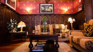 A room with a wooden ceiling, a sofa, a chair, a table, and wall-mounted lamps. - Hotel Palacete Real (Pilona)