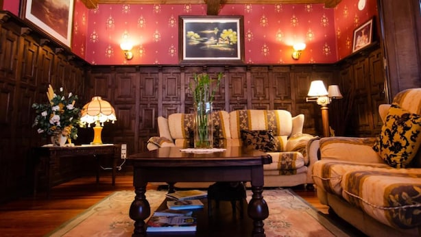 A room with a wooden ceiling, a sofa, a chair, a table, and wall-mounted lamps. - Hotel Palacete Real (Pilona)