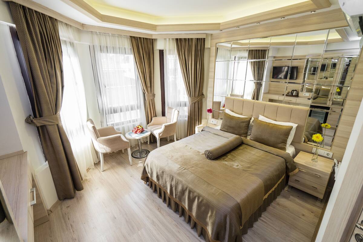 A modern bedroom with a large bed, a seating area with a table, and a built-in TV.