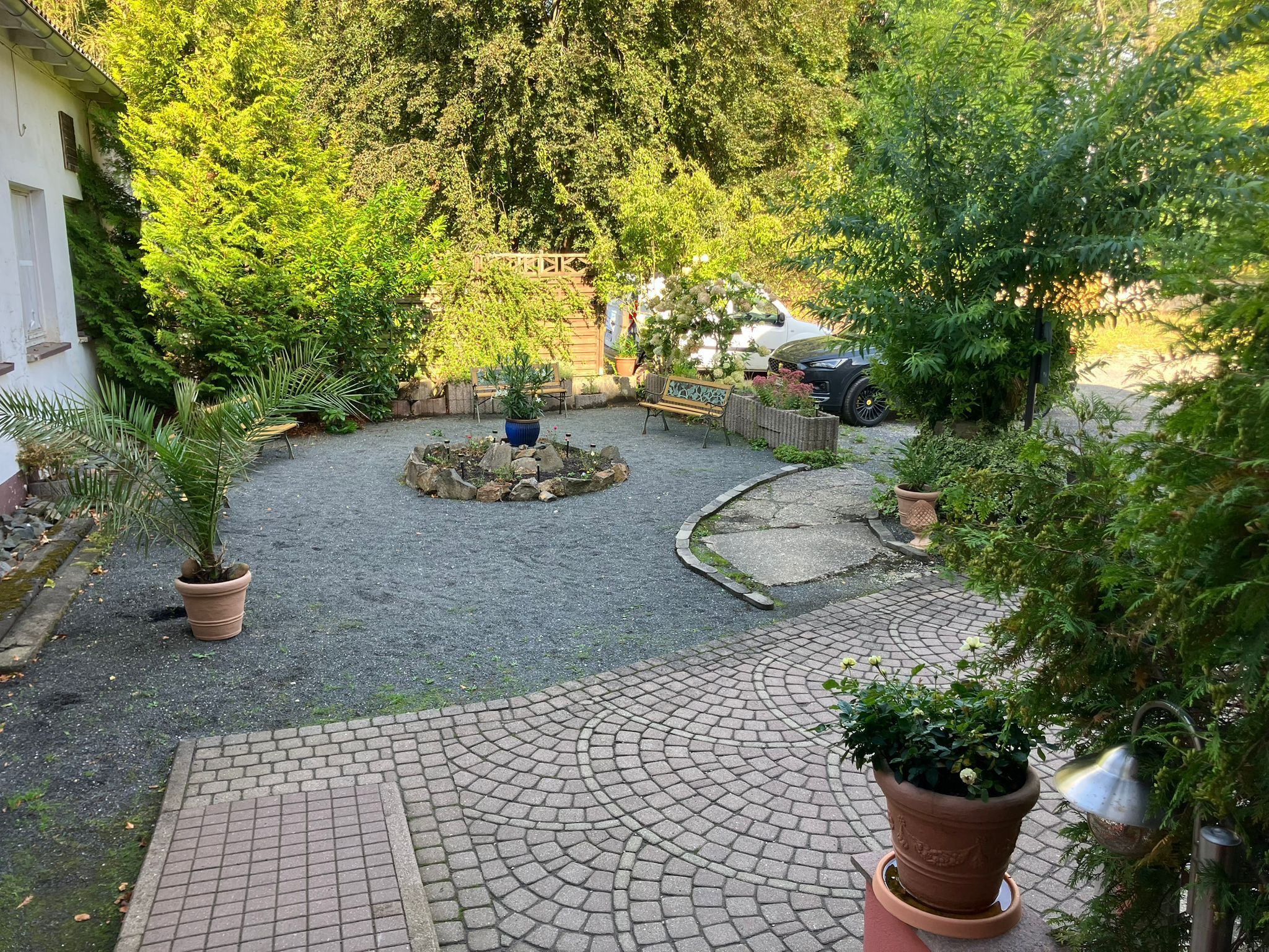 Ein Innenhof mit befestigtem Boden, einem runden Steinbrunnen und Blumentöpfen.