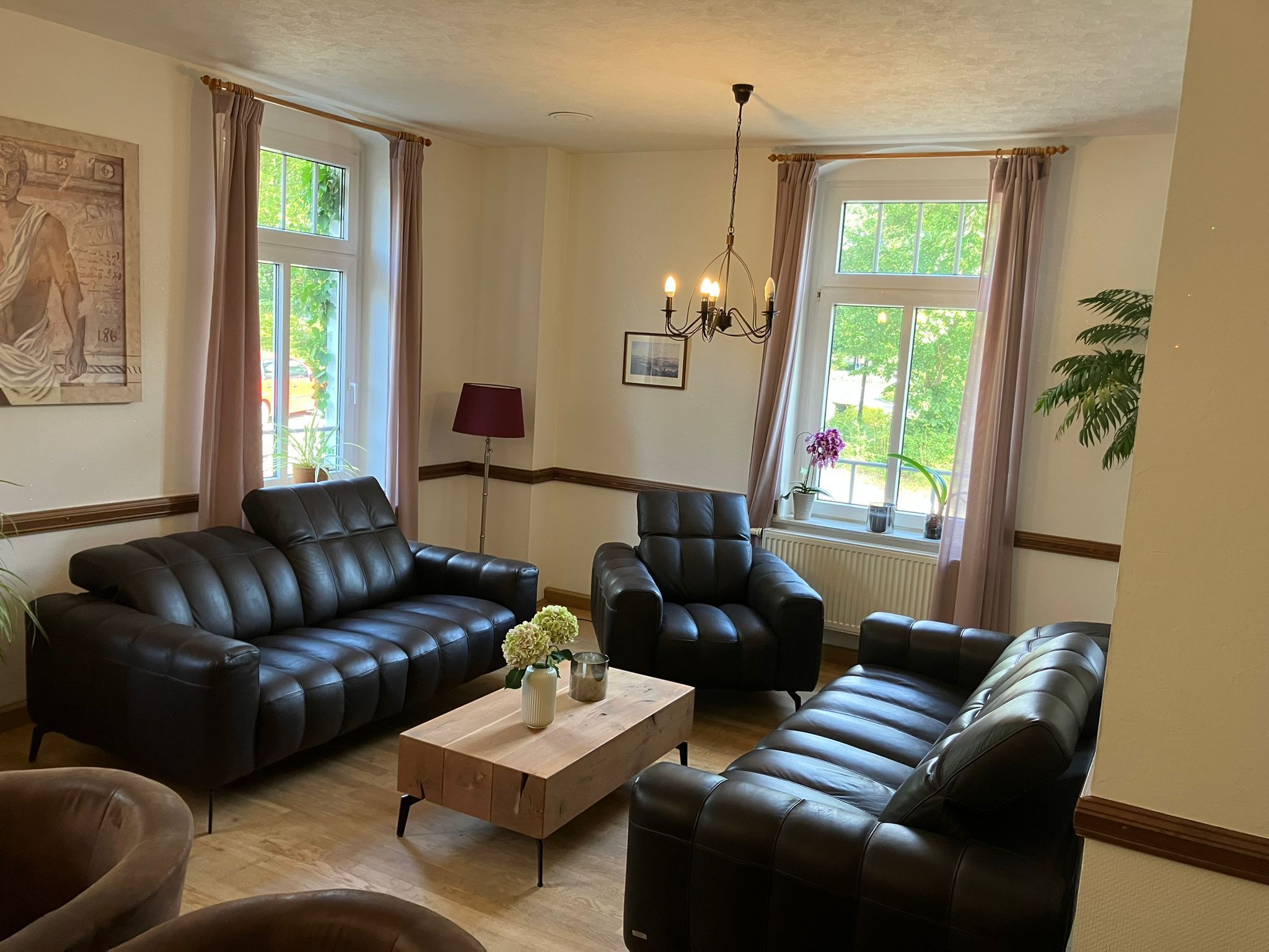 Ein Wohnzimmer mit zwei schwarzen Ledersofas, einem Holztisch mit einer Vase, einer Stehlampe und einem Bild an der Wand.