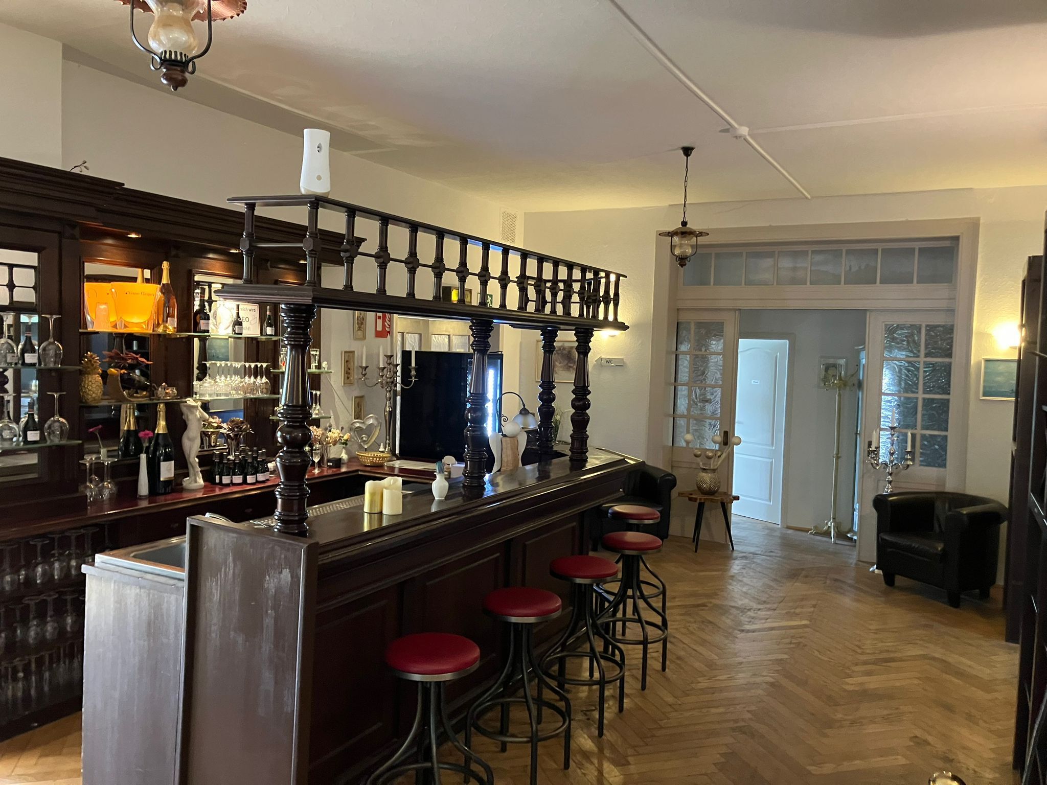 Eine Bar mit Holztresen, Barhocker sowie einer Auswahl an Flaschen und Gläsern.
