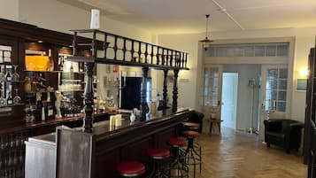 A bar area with a wooden counter, bar stools, and a variety of bottles and glasses.