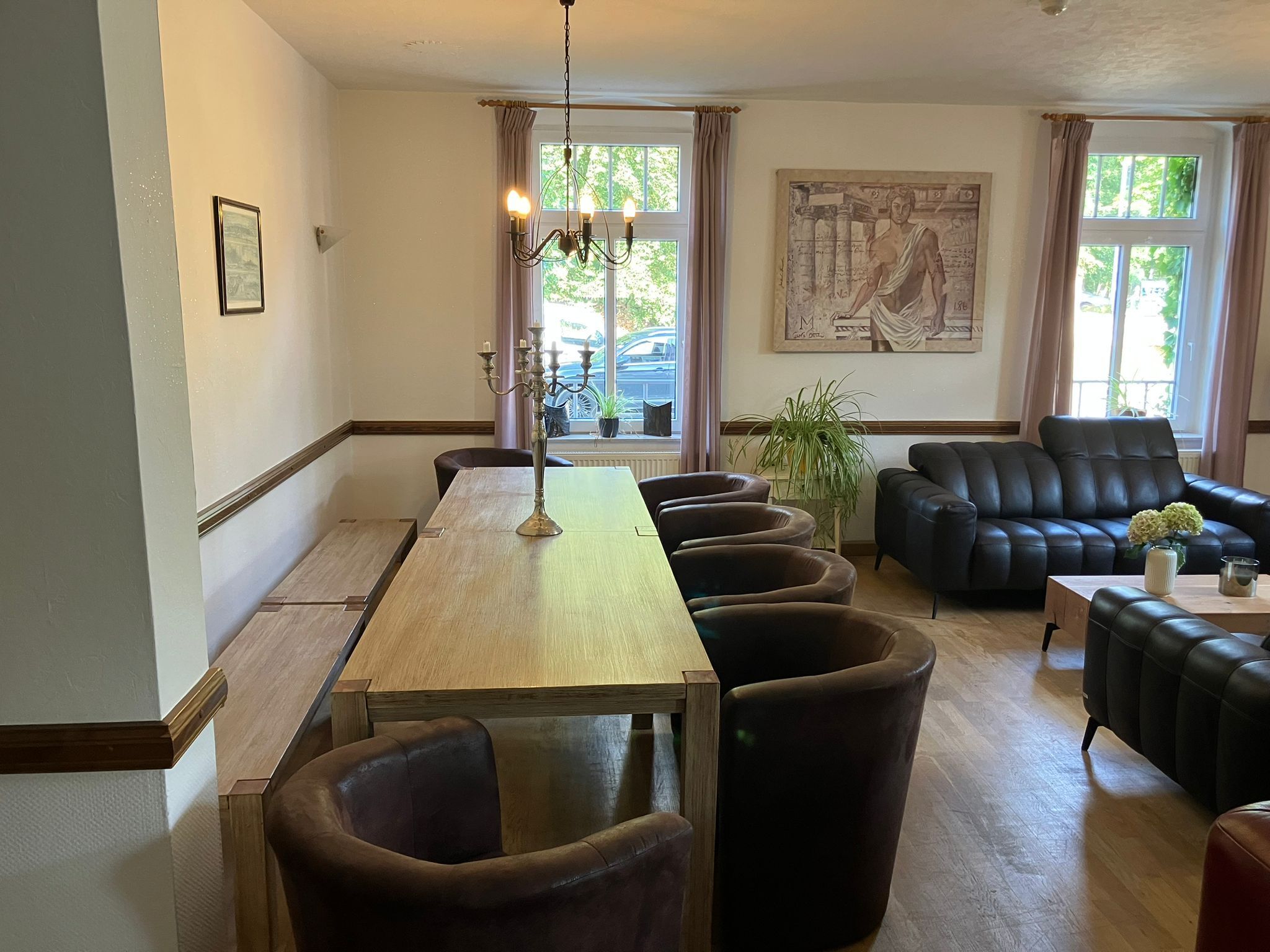 Una habitación con una larga mesa de madera, varias sillas de cuero, un sofá de cuero negro, un candelabro y un cuadro grande en la pared.
