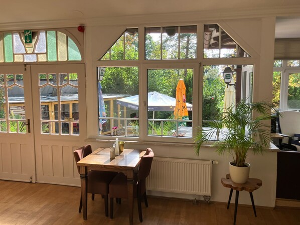 A dining area with a table and chairs, large windows with a view of the outdoors, and a potted plant.