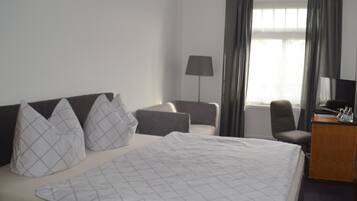 Habitación de hotel con cama, dos sillones, escritorio con lámpara y televisión.