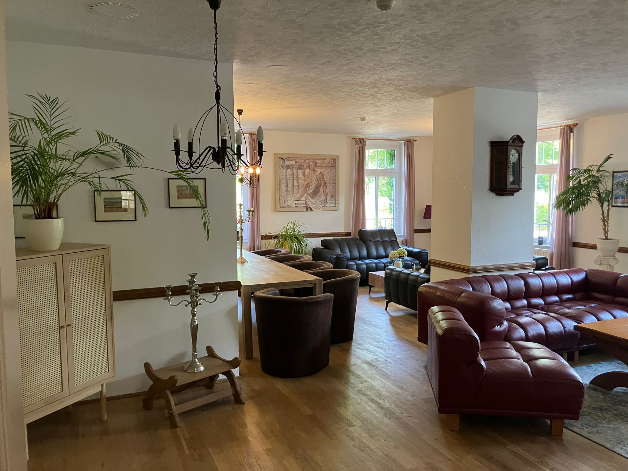 Un salon spacieux avec un grand canapé en cuir, une table basse en bois et un coin repas comprenant une table et des chaises en bois. On y trouve également des plantes en pot et un lustre.