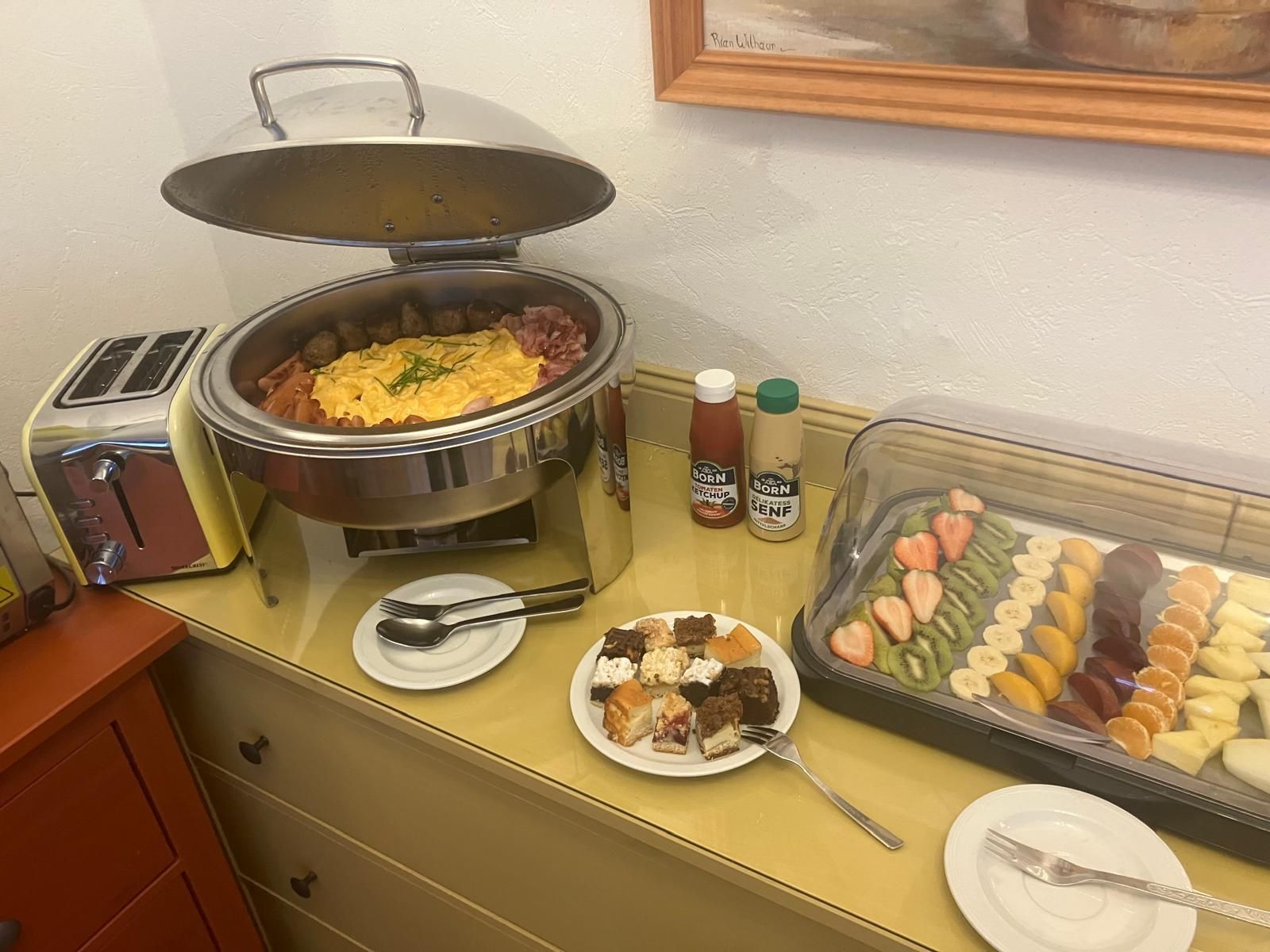 Montaje de bufé con una estación de comida caliente, salsas y una variedad de postres y frutas.