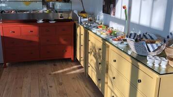 A modern kitchen with wooden flooring, a red cabinet, and a glass-top counter with various food items and kitchenware.