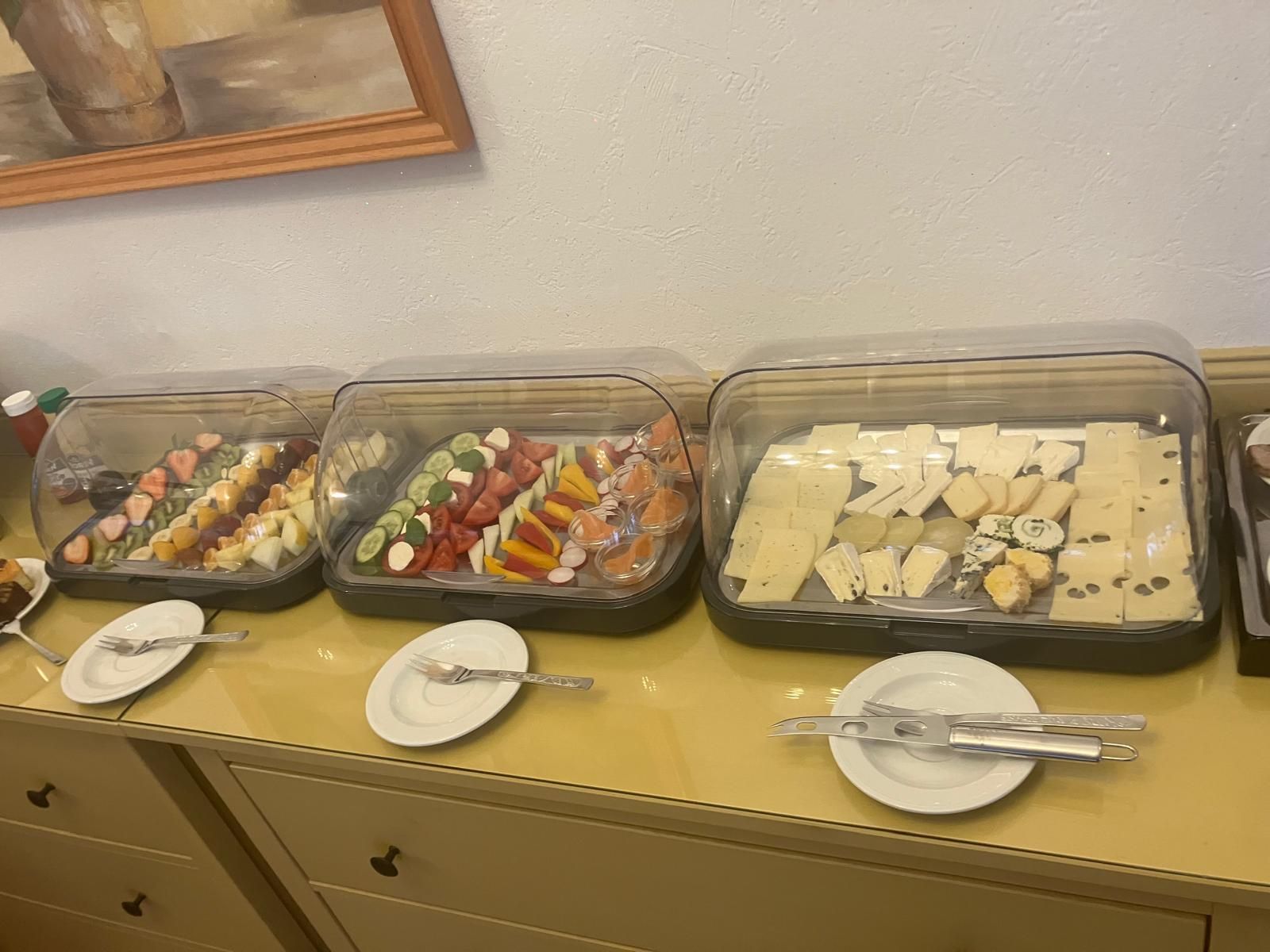 A buffet table with various food items in clear containers, accompanied by plates and cutlery.
