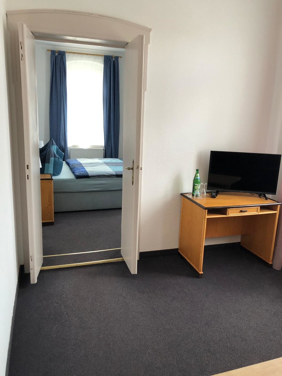 Una habitación de hotel con cama, escritorio con televisor y ventana con cortinas.