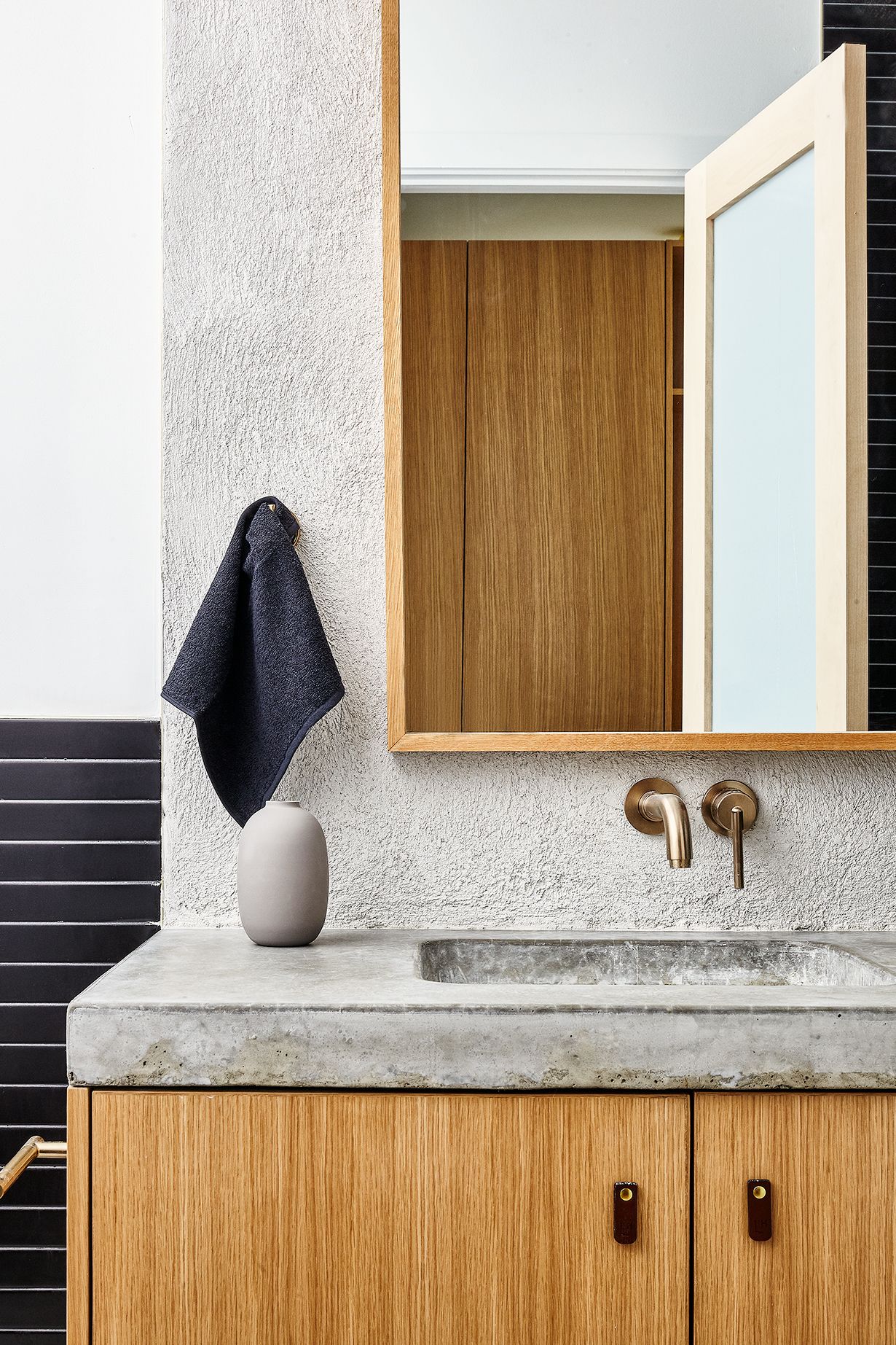 Un bagno con un piano in cemento, mobili in legno, un vaso bianco e un asciugamano appeso al muro.