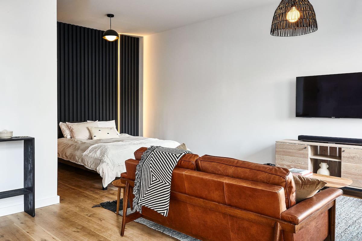 A modern bedroom with a bed, a leather sofa, a TV, and a pendant light.