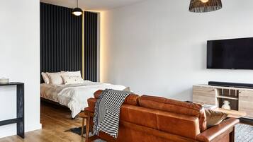 A modern bedroom with a bed, a leather sofa, a TV, and a pendant light.