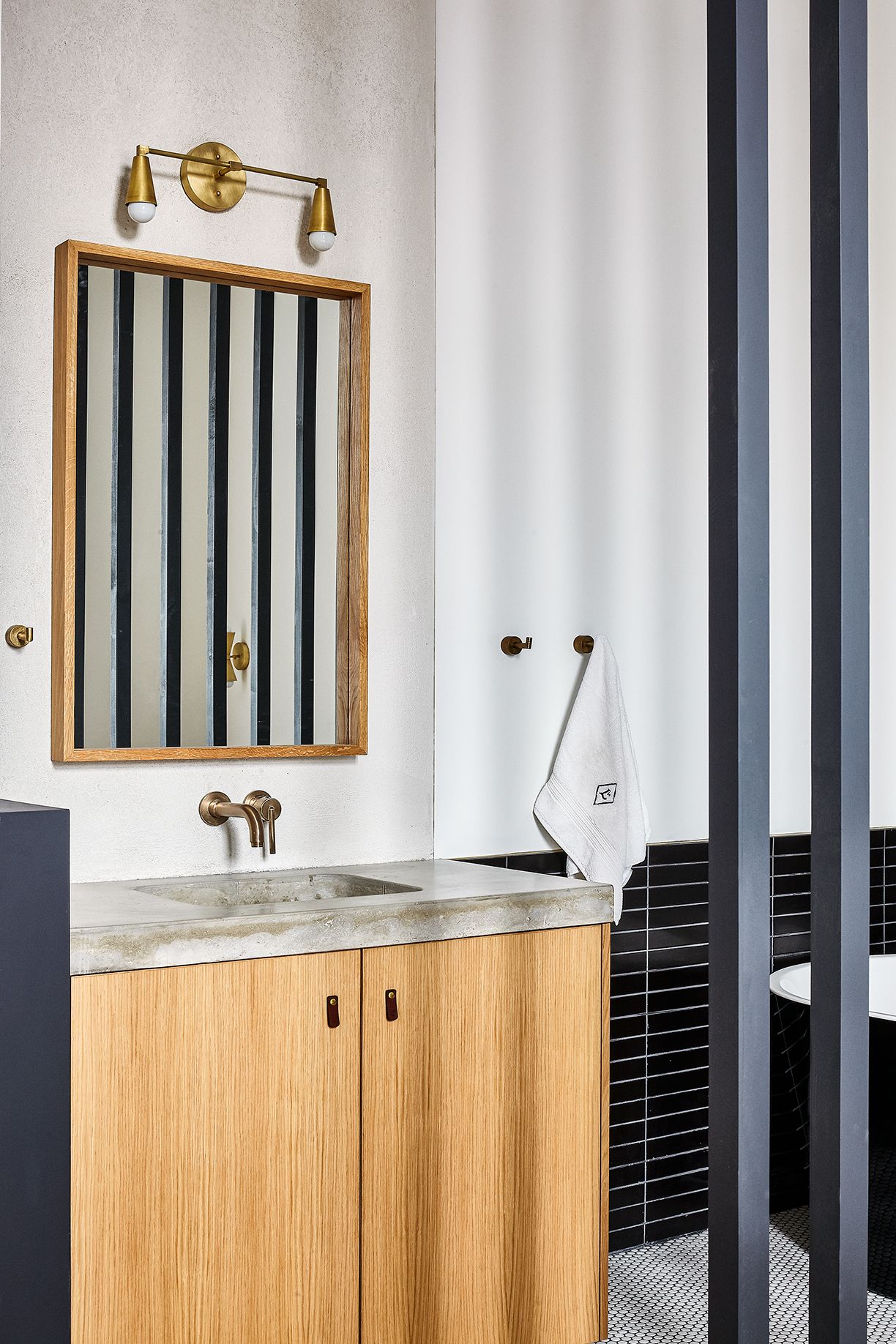 A modern bathroom with a wooden vanity, a large mirror, and a gold-colored wall-mounted light fixture.